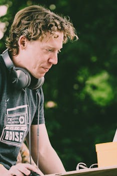 Young man DJ with headphones mixing music on a laptop outdoors.