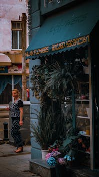 A quaint flower shop with lush plants on a city street, capturing urban charm with a passerby.