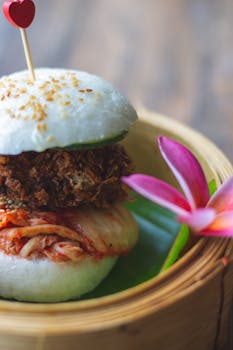Delicious bao bun with crispy filling, kimchi, sesame seeds, and flower garnish. Perfect for food enthusiasts.