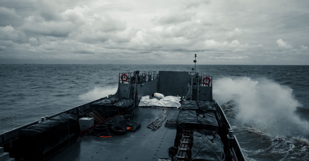 A military ship cruises through choppy ocean waters under a cloudy sky, showcasing naval power.