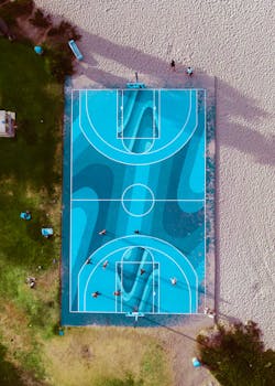 Top view of a colorful basketball court by the beach with players in action.
