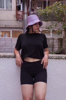 Woman in black outfit and bucket hat posing by a wall outdoors.