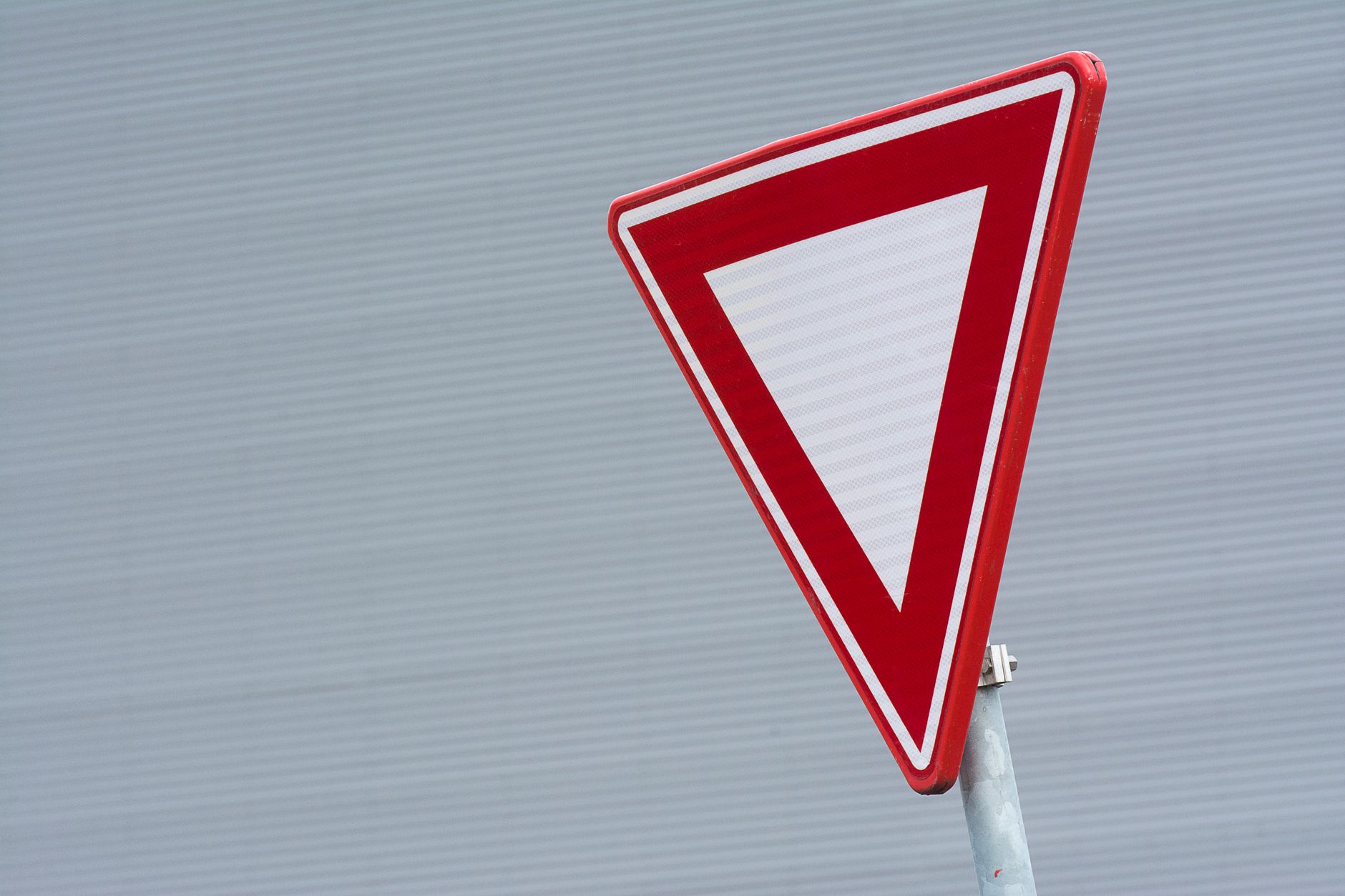 A close-up of a red yield traffic sign against a textured gray background.