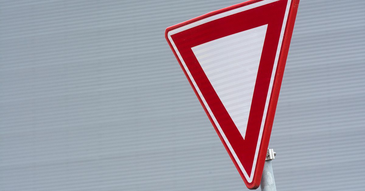 A close-up of a red yield traffic sign against a textured gray background.