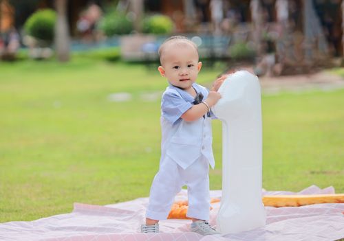 Free Cute baby standing with a balloon outdoors on a picnic blanket, perfect for birthday themes. Stock Photo
