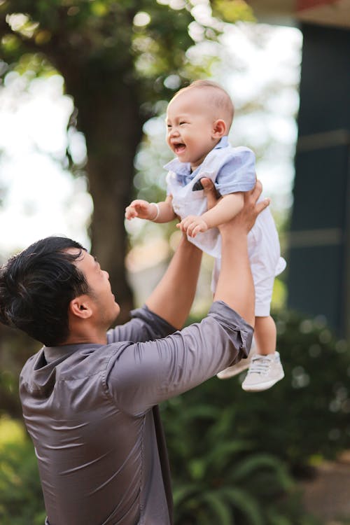 Man in Gray Long Sleeves Carrying a Happy Baby