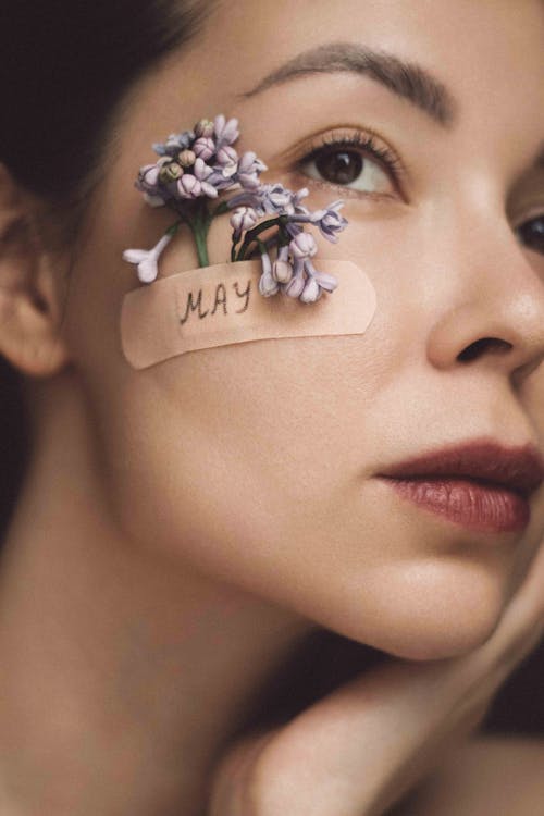 Close-up Portrait of a Woman with Flowers Tucked Behind a Band Aid Stuck to Her Cheek 