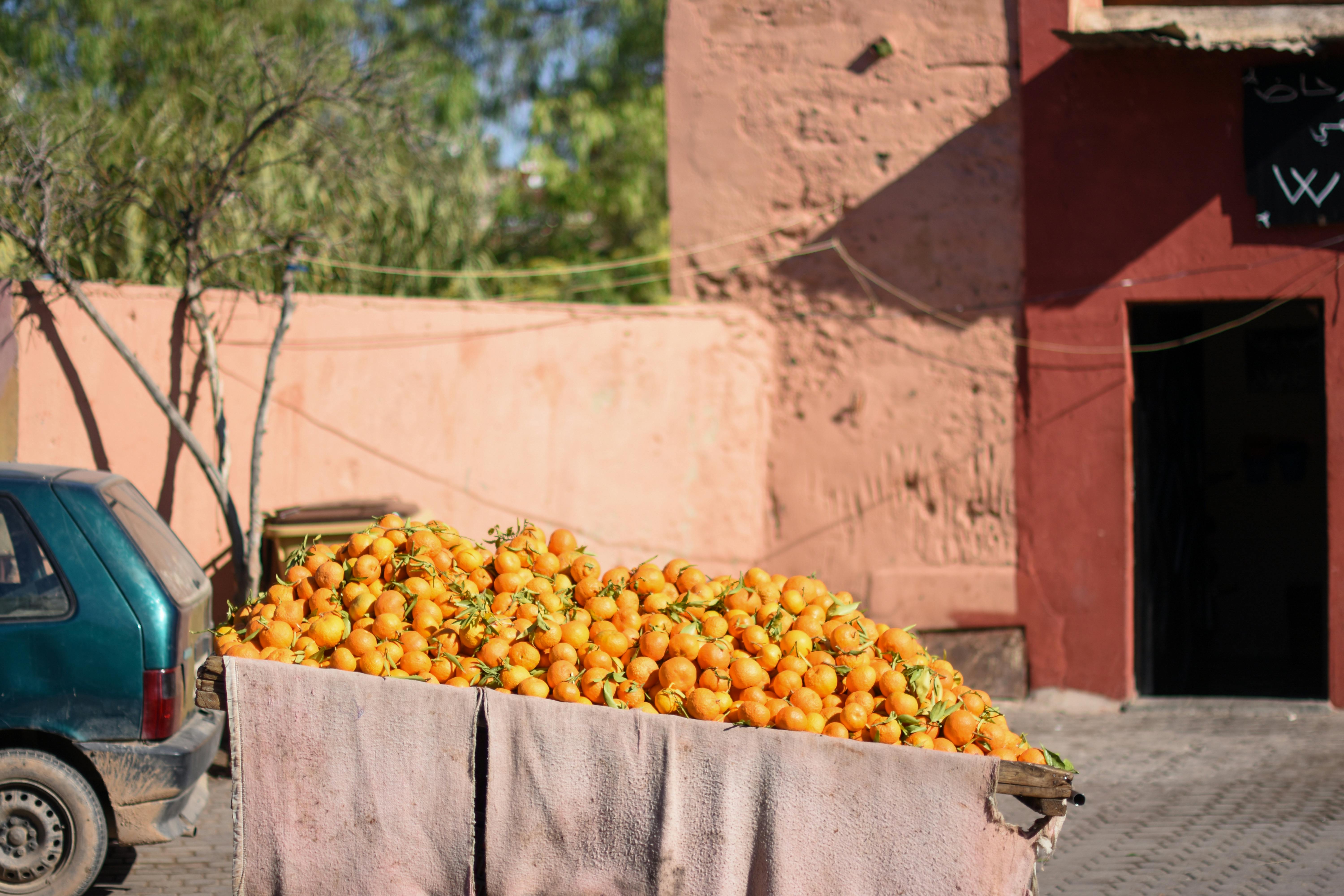 A cart filled with bright oranges on a sunny street in Marrakesh, Morocco, showcasing vibrant local culture.