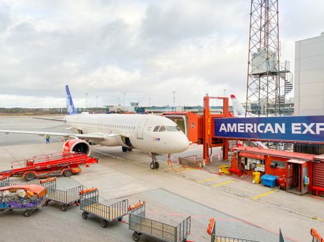 Aircraft docked at Stockholm Arlanda Airport gate with ground crew and equipment.