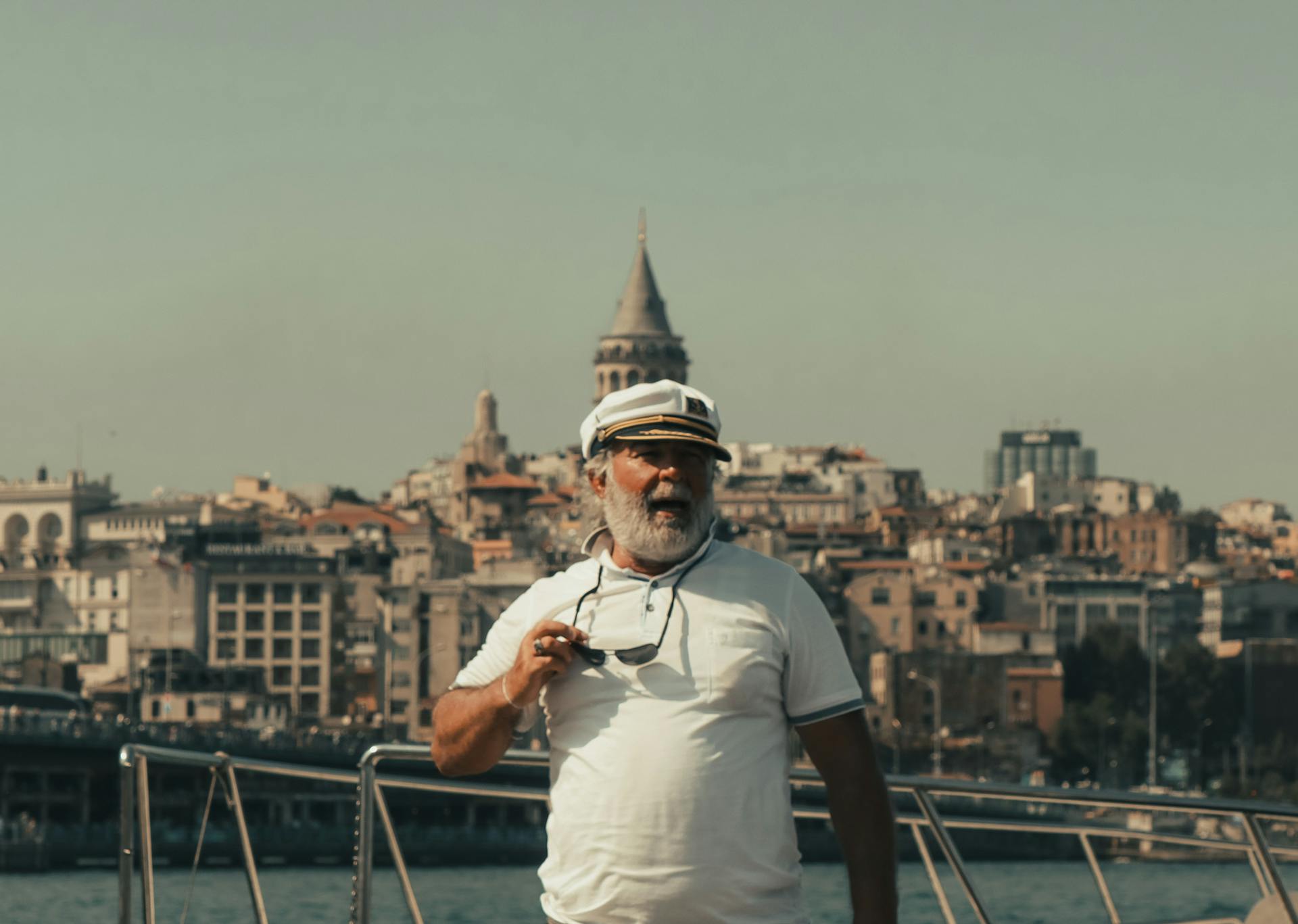 Elderly bearded sailor posing with sunglasses on a boat in front of Galata Tower.