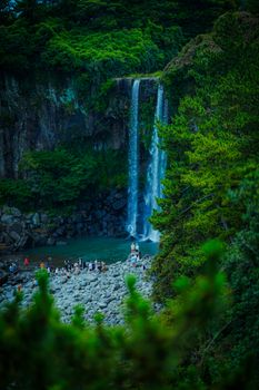Majestic waterfall cascading in green South Korean forest with tourists admiring the view.