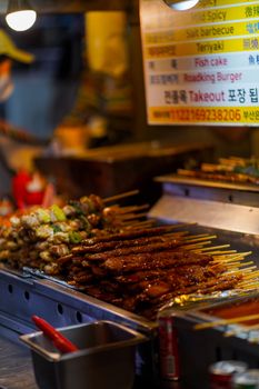 A vibrant display of grilled skewers and barbecue at a bustling Korean street food stall.