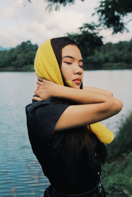 Free A serene woman wearing a yellow scarf meditates by a tranquil lake, embodying peace and nature. Stock Photo