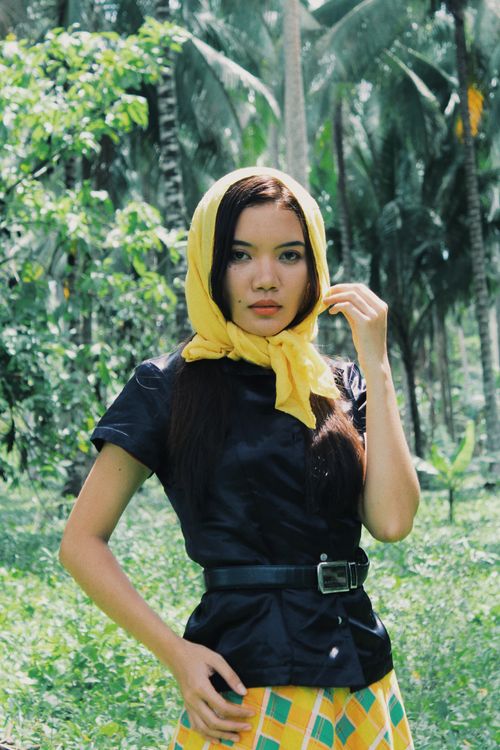 Free A young woman in a tropical forest wearing a vibrant yellow headscarf. She is dressed in a black top and colorful skirt. Stock Photo
