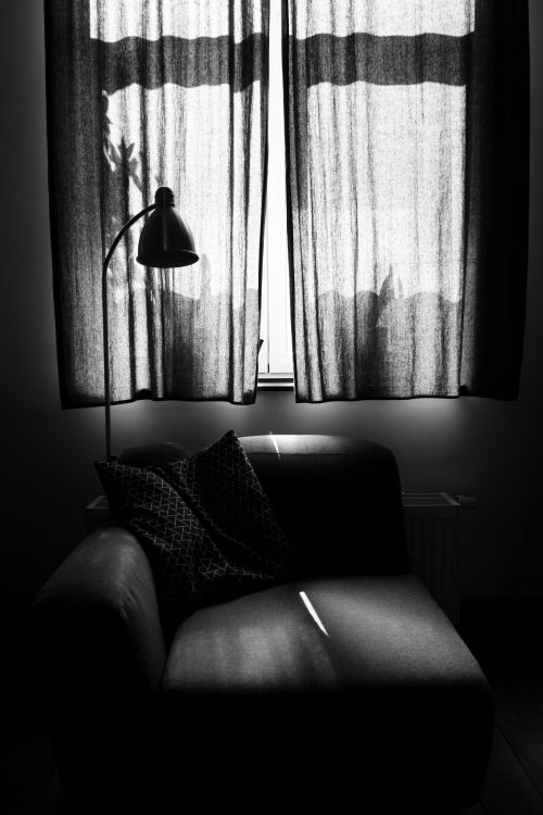 Free Elegant black and white interior with sofa and lamp casting artistic shadows on curtains. Stock Photo