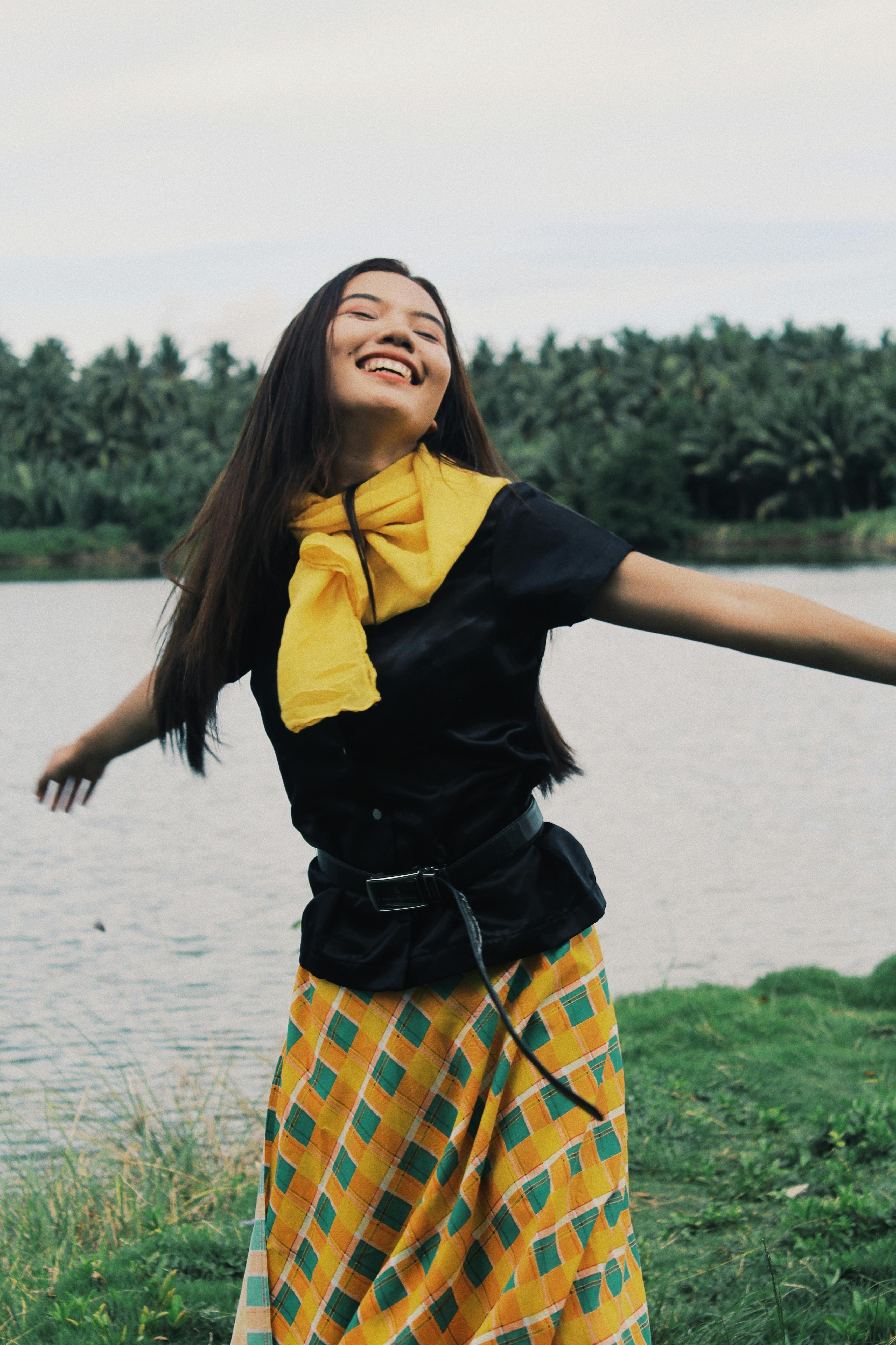 Smiling woman with arms outstretched enjoying nature by a serene lake.