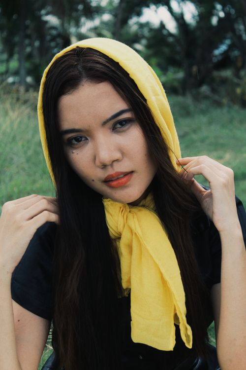 Free Asian woman posing outdoors, wearing a yellow scarf, with a natural green background. Stock Photo