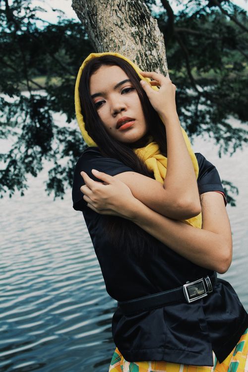 Free A stylish portrait of a woman in a hijab leaning against a tree by a calm lake. Stock Photo
