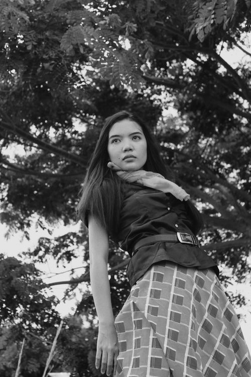Free Black and white low angle portrait of a stylish woman with trees in the background, exuding modern fashion. Stock Photo