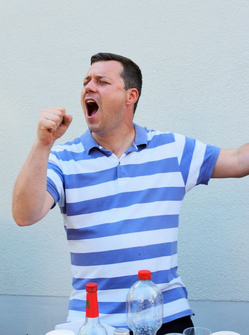Free Energetic caucasian man in a striped shirt singing outdoors, capturing a joyful moment. Stock Photo