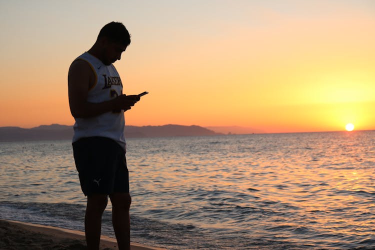 Man In White Jersey Holding A Cellphone At The Beach