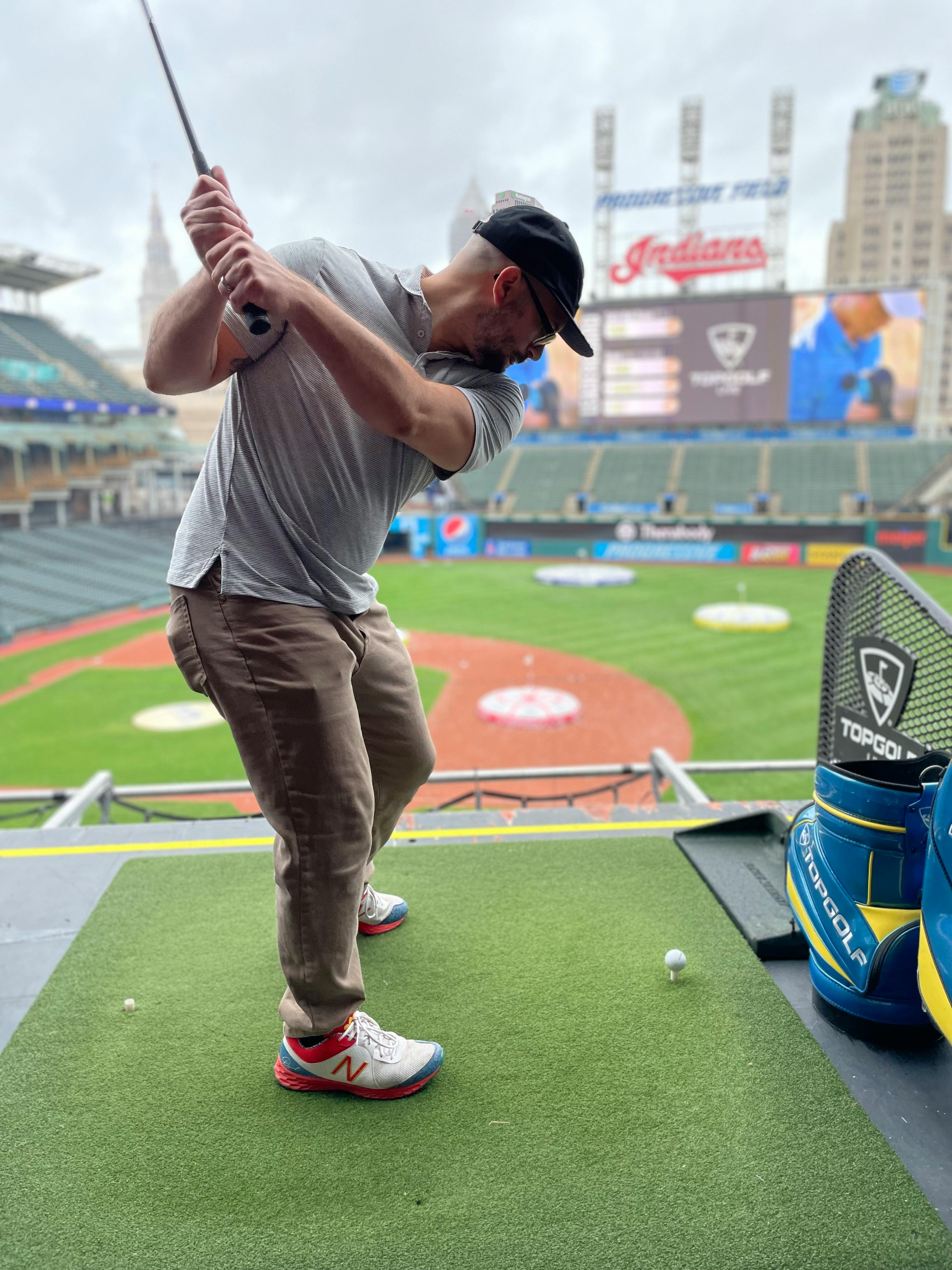 Man practicing golf swing at a baseball stadium golf range in Cleveland.