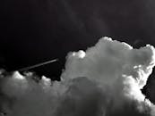 一张黑白图像中，一架飞机飞过云层密布的戏剧性天空
