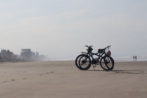 Free Two bicycles parked on a serene beach with distant skyline. Ideal for travel and lifestyle visuals. Stock Photo