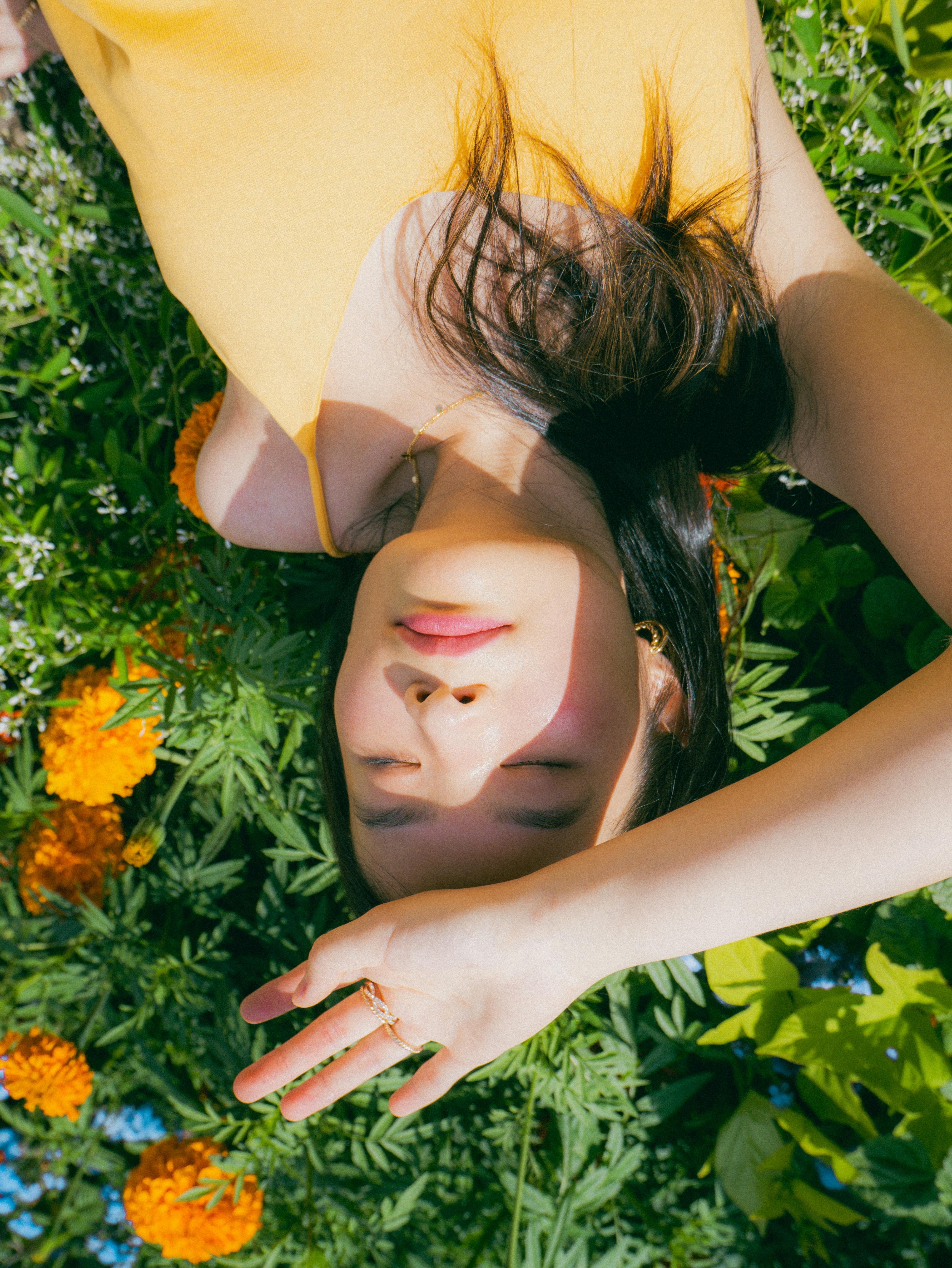 Relaxed woman lying on grass with eyes closed, surrounded by colorful flowers.