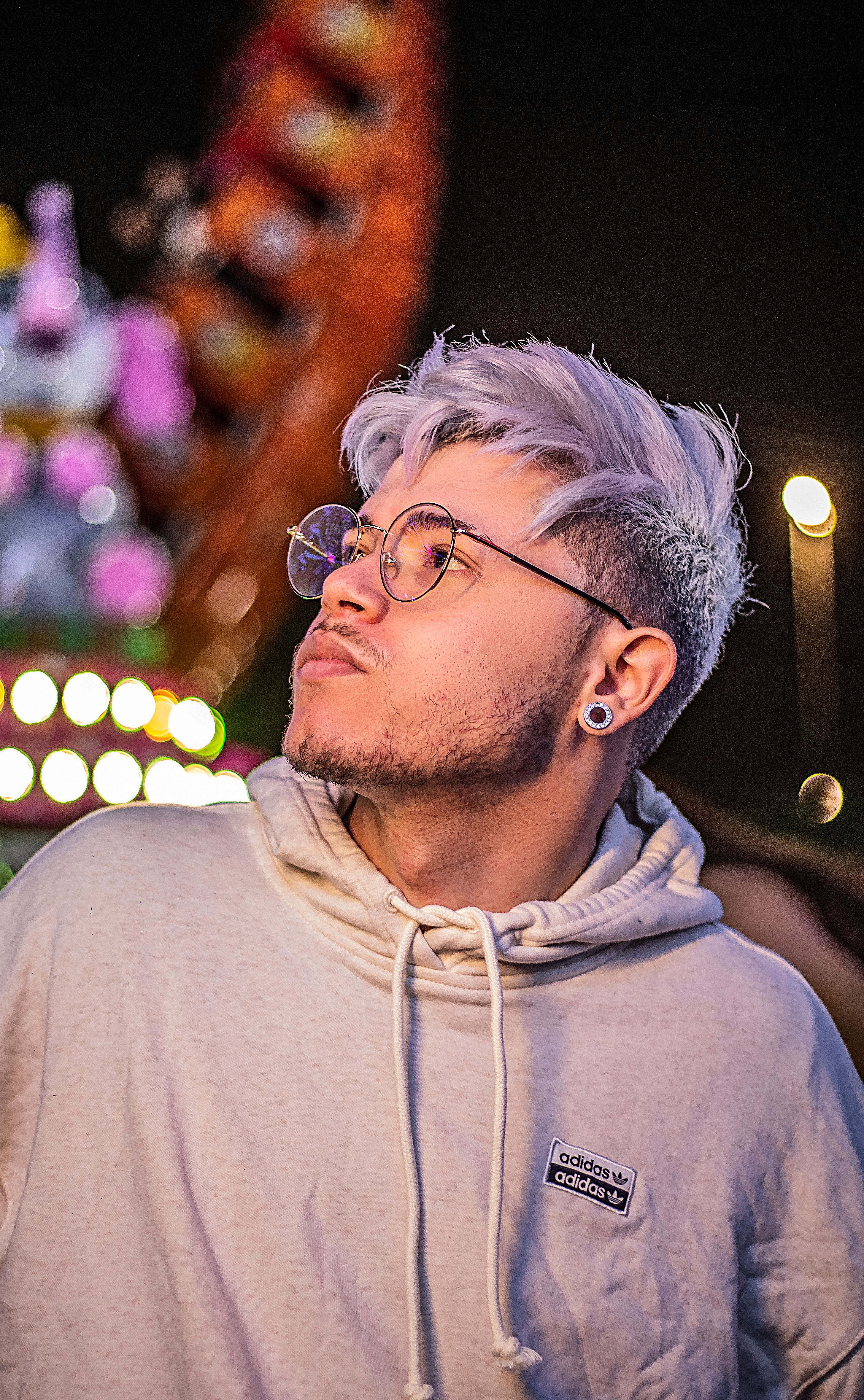 Stylish young man with purple hair and hoodie at a vibrant night carnival in São Paulo.