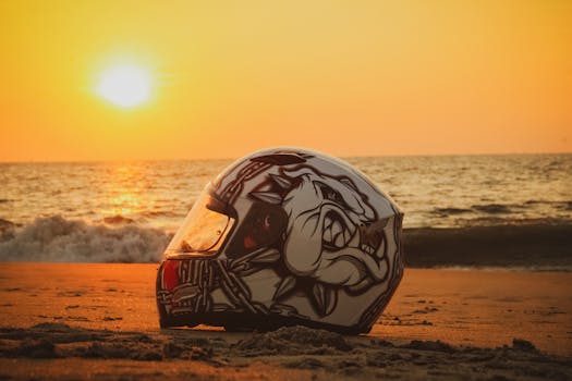 A detailed motorcycle helmet sits on a sandy beach during a breathtaking sunset in India.
