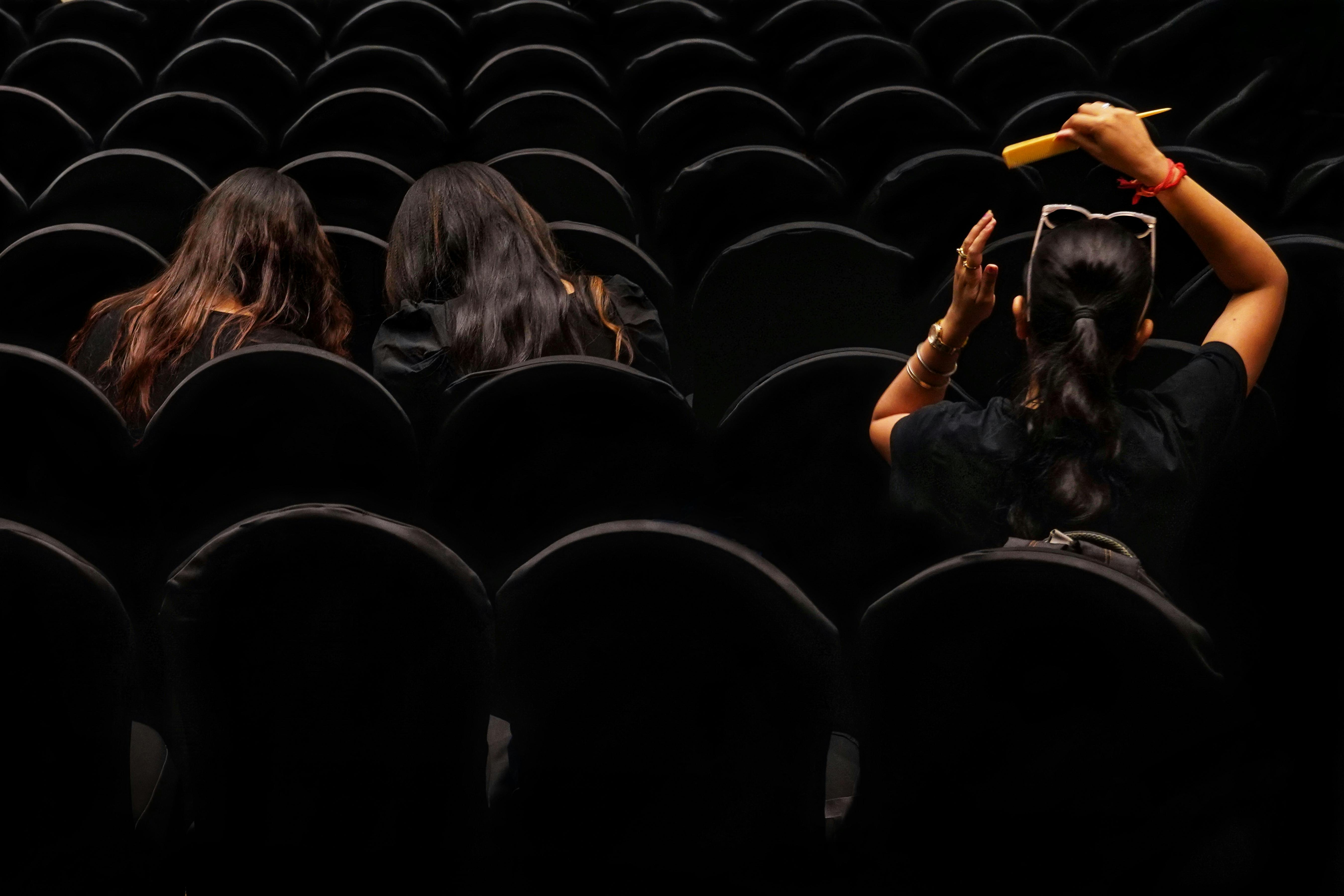 Free Three women seated in a cinema auditorium with patterned empty seats in Kolkata, India. Stock Photo