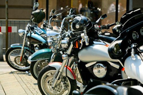 Free A close-up view of multiple parked motorcycles lined up in a sunny urban environment. Stock Photo