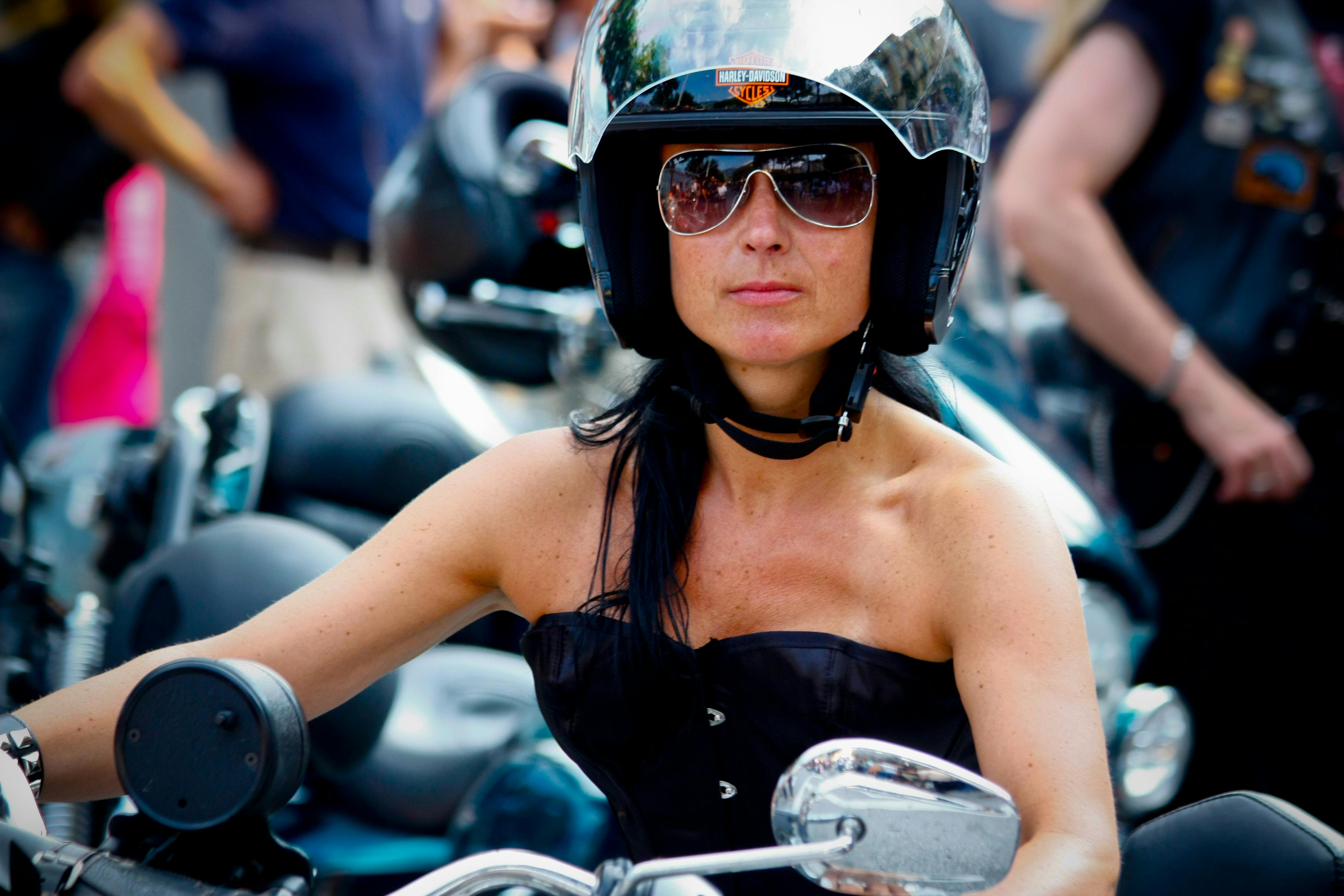 Strong woman in helmet and sunglasses riding a motorcycle confidently outdoors.
