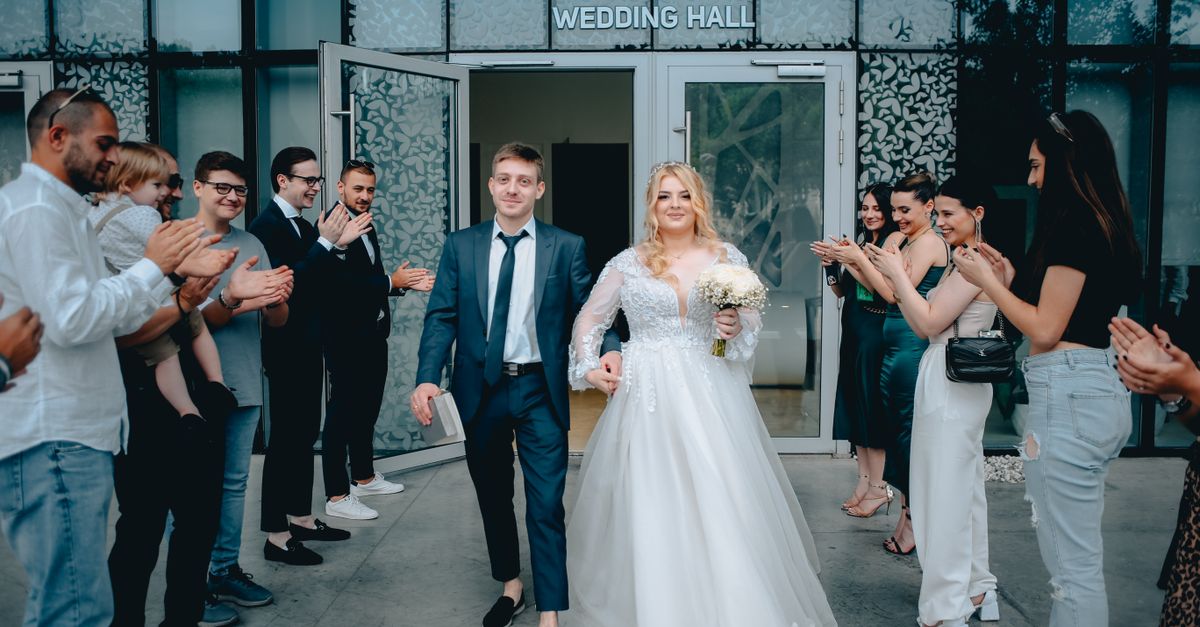 Newlywed couple exiting wedding hall, greeted by applauding guests in celebration.