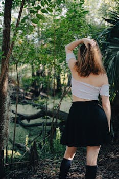 Back view of a woman in a black skirt and crop top standing in a vibrant forest