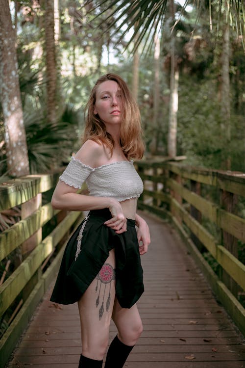 Woman in White Top and Black Skirt Posing on a Wooden Bridge