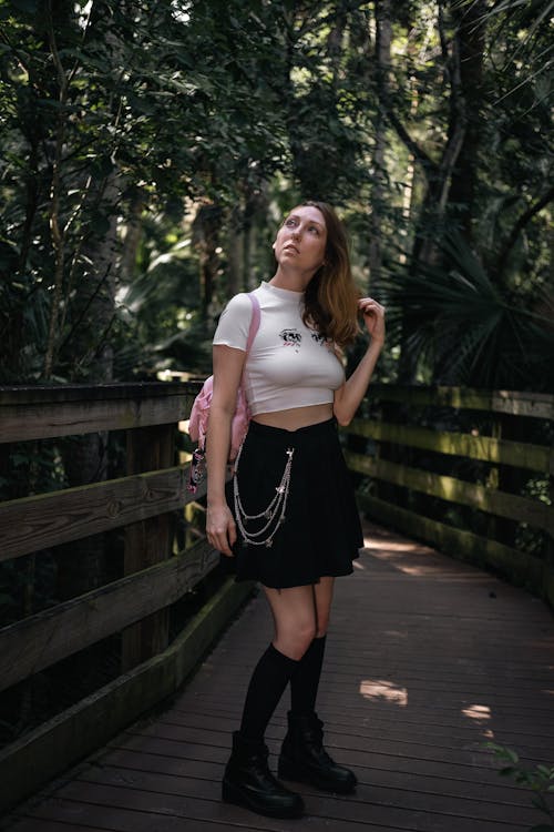 A Woman in Black Skirt and Shoes Standing on a Wooden Bridge while Looking Up