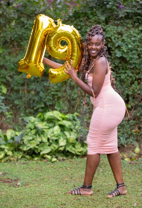A Woman in a Pink Dress Holding Number Balloons