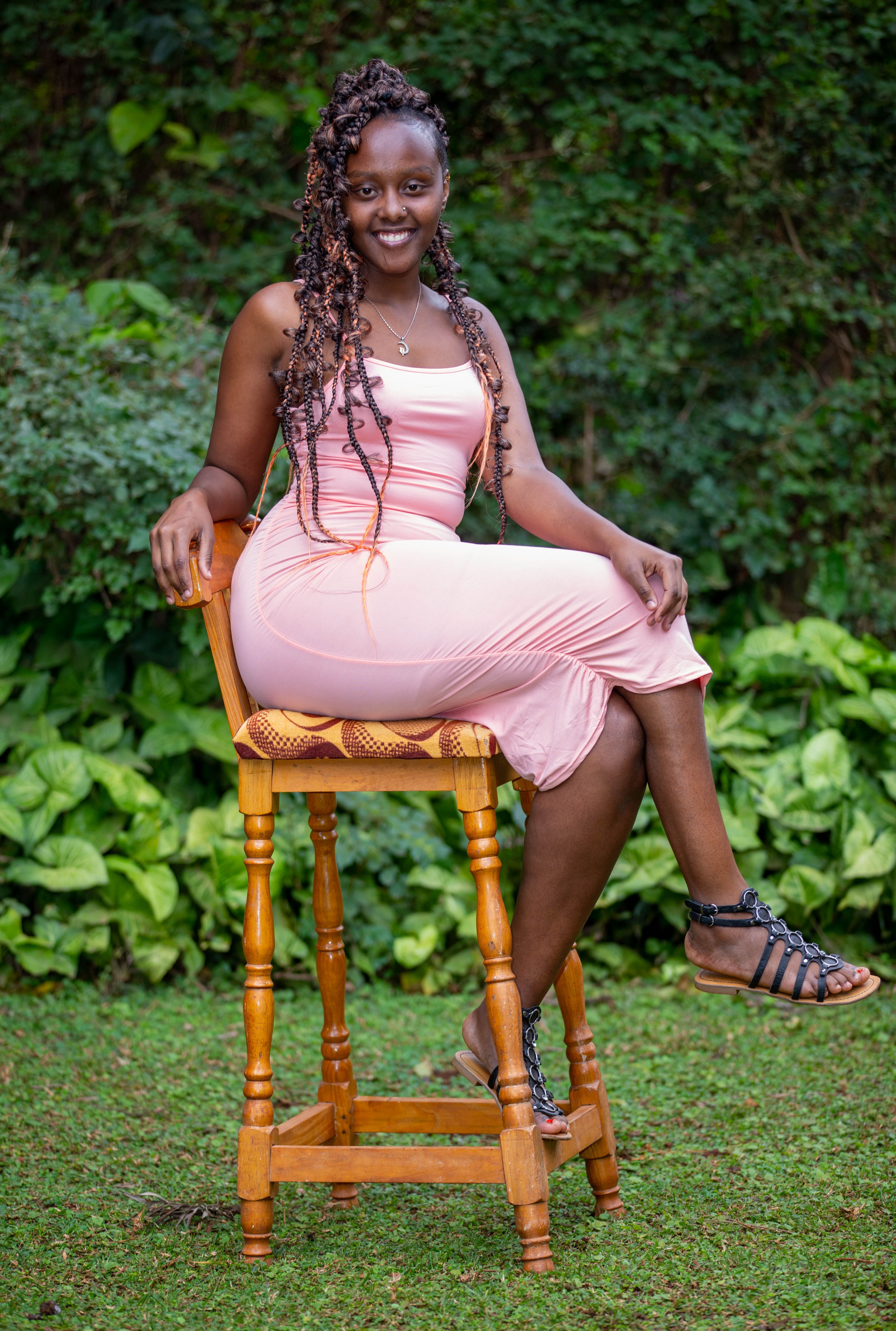 Fashionable woman with dreadlocks smiling while sitting on a wooden chair in a garden setting.