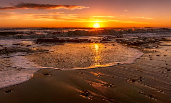 Beautiful beach sunset with waves crashing on the shore, golden light reflecting.