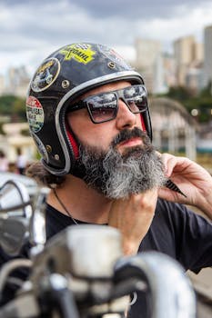 Close-up of a bearded man adjusting his motorcycle helmet against an urban backdrop.