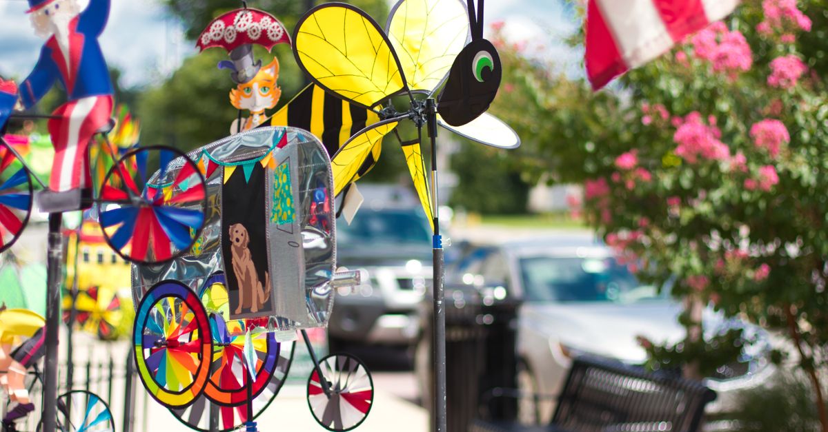 Brightly colored wind spinners on display in an outdoor garden setting alongside flowers and an American flag.