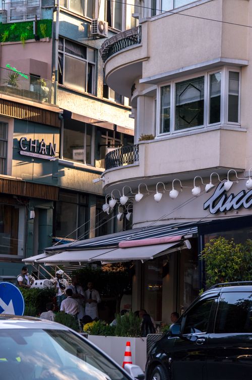 Free A lively city street corner featuring a modern cafe with outdoor seating, capturing urban life. Stock Photo