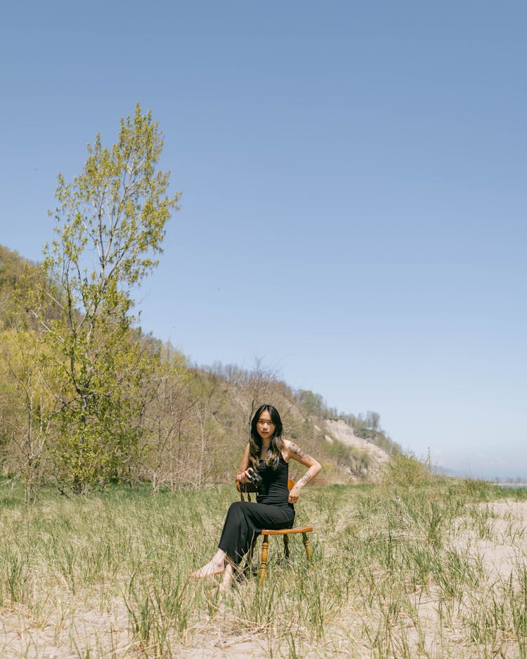 Portrait Of A Woman In Black Clothes Sitting In Field On A Chair In Summer