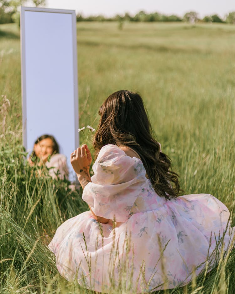 Girl Wearing A Pastel Dress Sitting In Grass Field With A Mirror