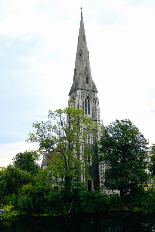 Free St. Alban's Church steeple surrounded by lush greenery in Copenhagen. Stock Photo