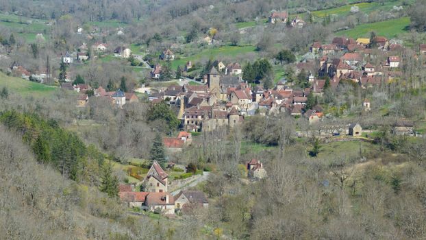 Aerial view of a picturesque European village surrounded by lush greenery and hilly terrain.