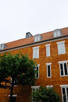 Low angle view of an orange brick apartment building with a tree in front, showcasing European architecture.