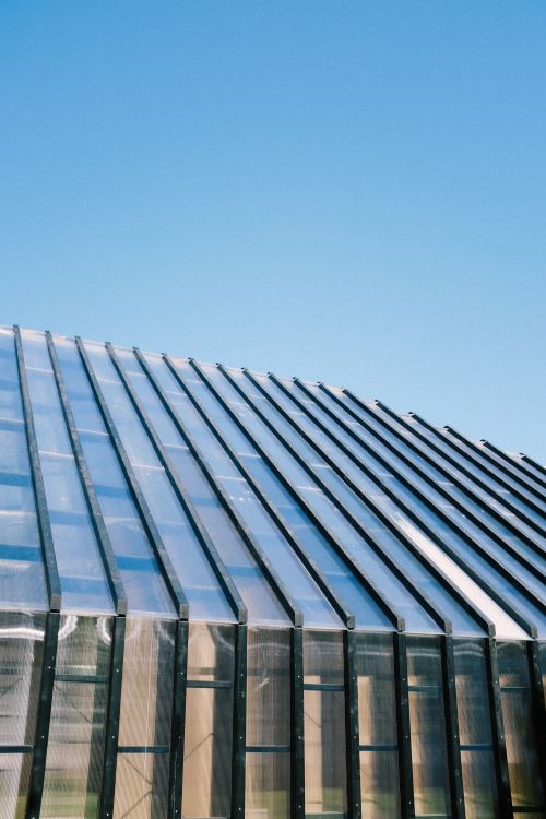 Free A modern architectural structure with glass panels and metal framework under a clear blue sky. Stock Photo